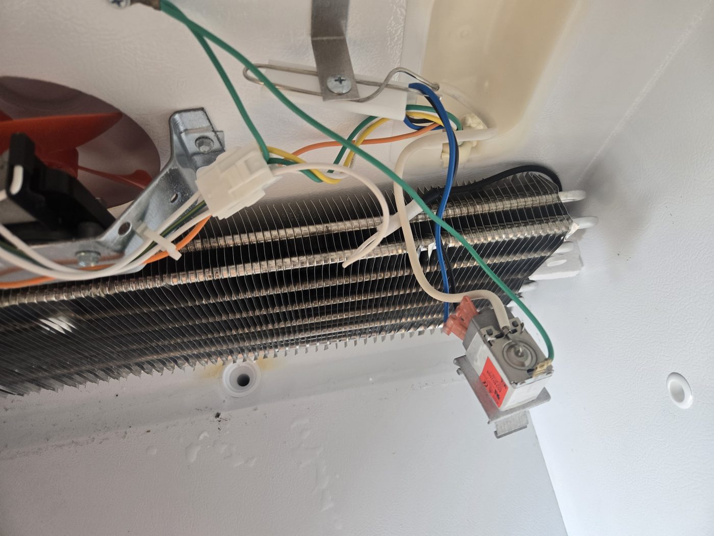 Frost-covered evaporator coils behind a refrigerator panel